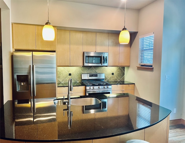 kitchen featuring dark stone countertops, decorative light fixtures, appliances with stainless steel finishes, and light wood-type flooring