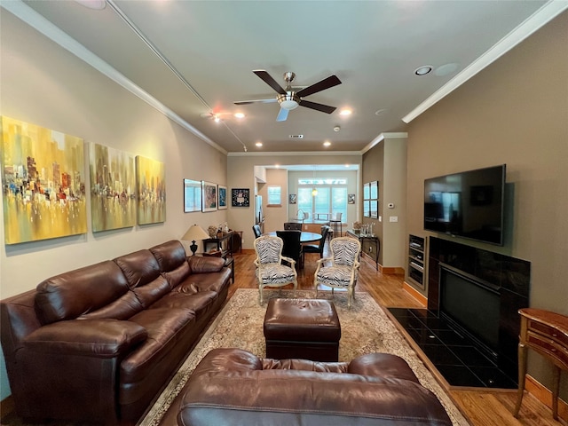 living room with a tiled fireplace, crown molding, ceiling fan, and dark hardwood / wood-style floors