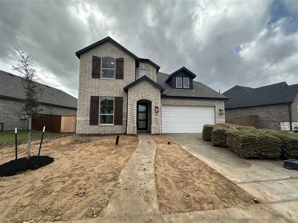 traditional home featuring a garage, driveway, brick siding, and fence