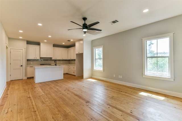 kitchen with light wood-type flooring, ceiling fan, a kitchen island with sink, sink, and white cabinetry