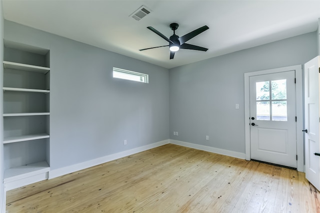 unfurnished room featuring built in shelves, light hardwood / wood-style flooring, and ceiling fan