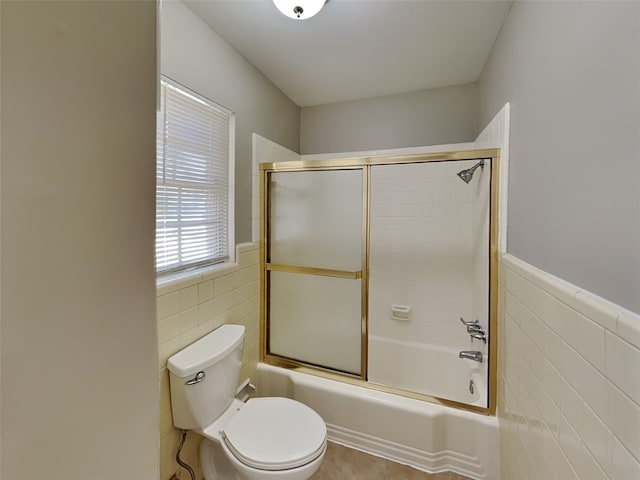 bathroom featuring tile walls, shower / bath combination with glass door, and toilet