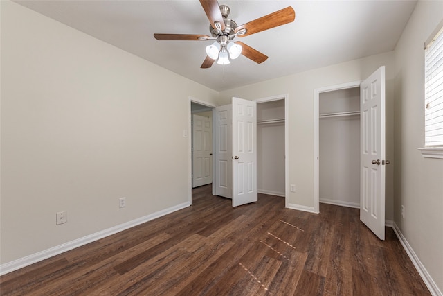 unfurnished bedroom featuring dark hardwood / wood-style floors, ceiling fan, and multiple closets