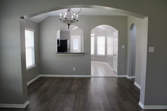 unfurnished dining area with lofted ceiling, dark wood-type flooring, and an inviting chandelier