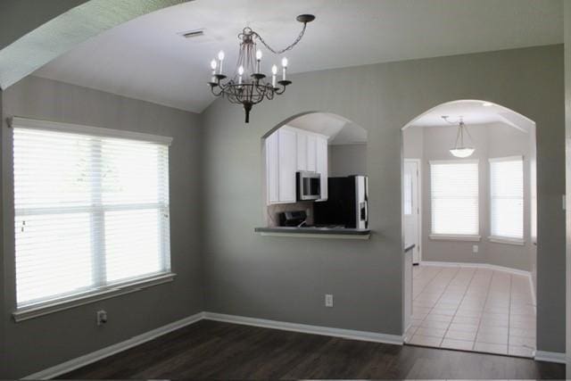 unfurnished dining area featuring lofted ceiling, a chandelier, and dark hardwood / wood-style flooring