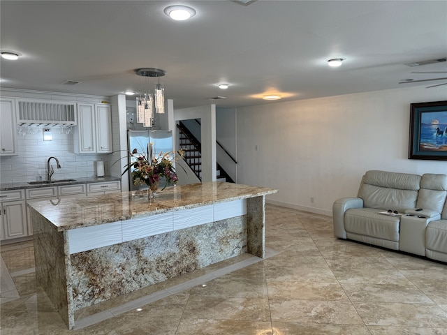 kitchen featuring an island with sink, stainless steel fridge, sink, decorative light fixtures, and white cabinetry