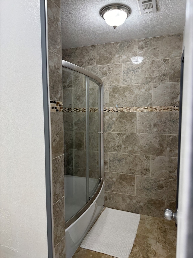 bathroom with a textured ceiling and combined bath / shower with glass door