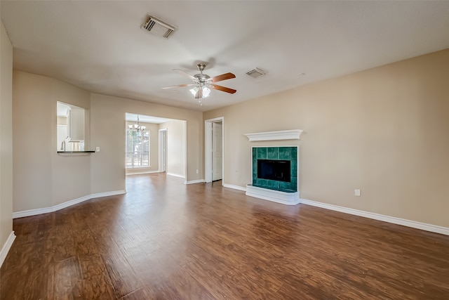 unfurnished living room featuring ceiling fan with notable chandelier, dark wood-type flooring, and a tile fireplace