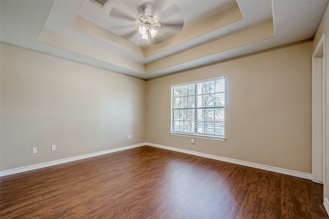 empty room with dark wood-type flooring, a tray ceiling, and ceiling fan