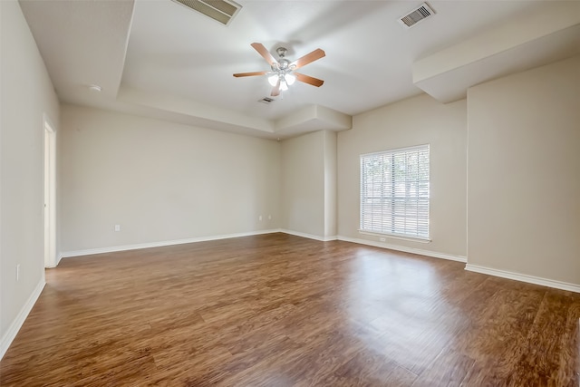 spare room with dark wood-type flooring, ceiling fan, and a raised ceiling