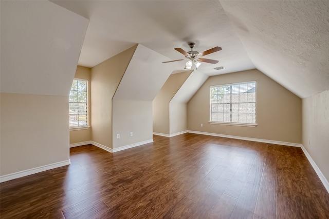 additional living space featuring lofted ceiling, a textured ceiling, dark hardwood / wood-style floors, and a healthy amount of sunlight