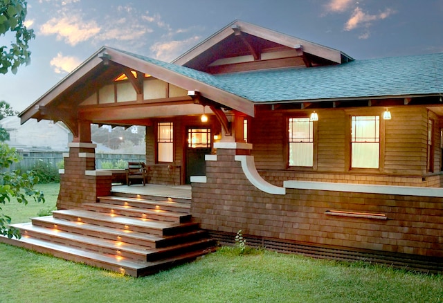 back house at dusk featuring a lawn