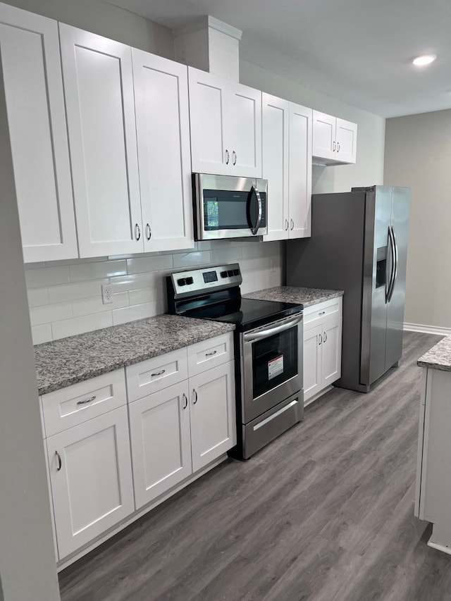 kitchen with decorative backsplash, white cabinetry, light stone countertops, dark hardwood / wood-style flooring, and stainless steel appliances