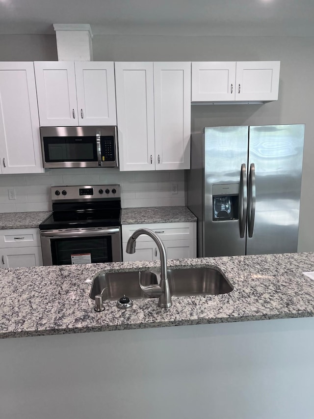 kitchen with backsplash, appliances with stainless steel finishes, light stone countertops, a sink, and white cabinetry