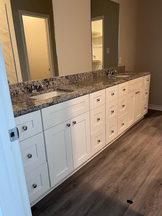 full bathroom with double vanity, a sink, baseboards, and wood finished floors