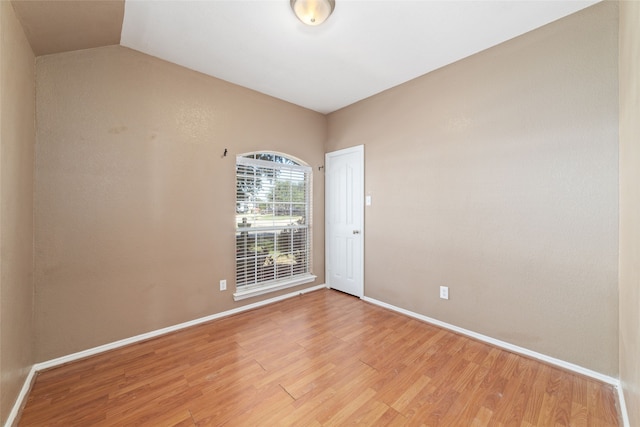 spare room featuring wood-type flooring and vaulted ceiling