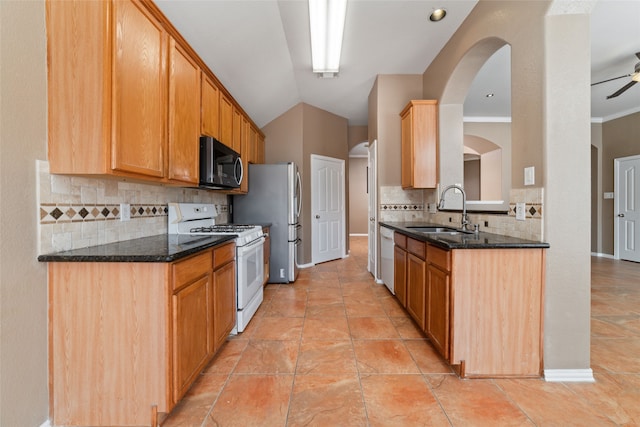 kitchen featuring sink, backsplash, white gas range oven, stainless steel refrigerator, and dark stone counters