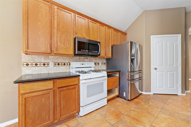 kitchen featuring lofted ceiling, light tile patterned floors, backsplash, appliances with stainless steel finishes, and dark stone countertops