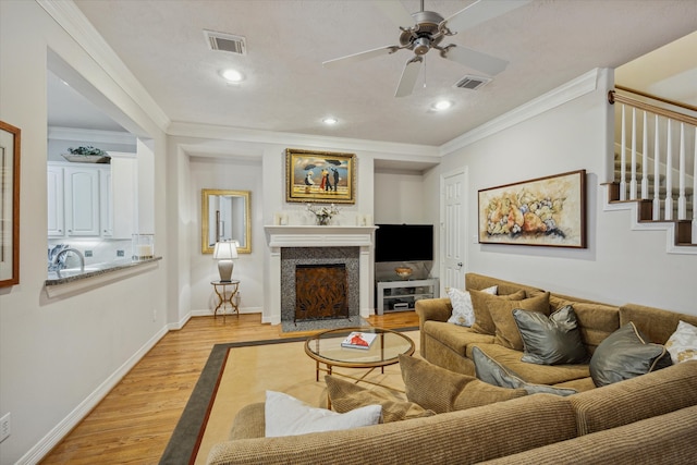 living room with light wood-type flooring, ceiling fan, ornamental molding, and a premium fireplace