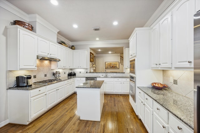 kitchen featuring dark stone counters, hardwood / wood-style flooring, appliances with stainless steel finishes, a kitchen island, and white cabinetry