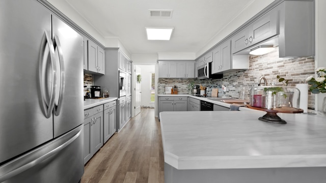 kitchen featuring gray cabinetry, ornamental molding, light hardwood / wood-style floors, stainless steel appliances, and decorative backsplash