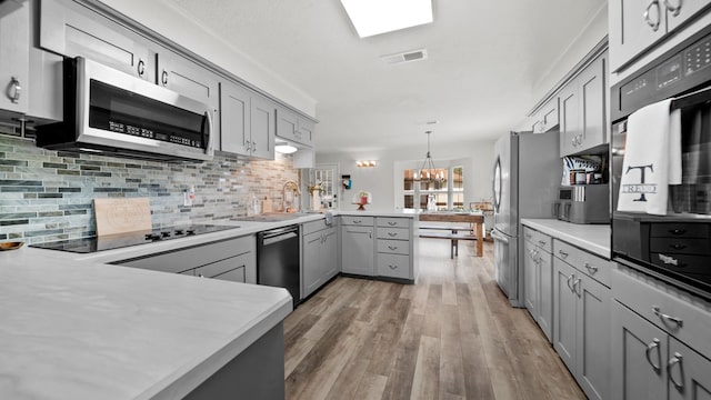 kitchen with kitchen peninsula, hardwood / wood-style floors, black appliances, pendant lighting, and gray cabinetry