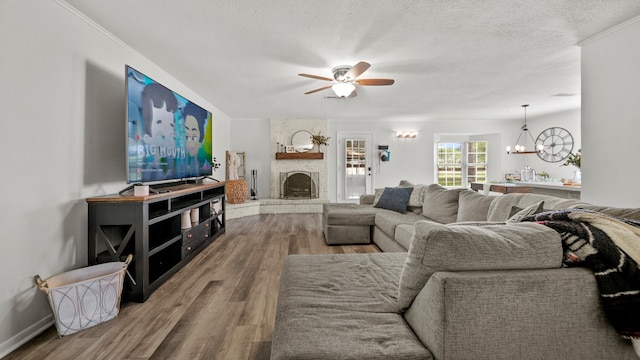 living room with ceiling fan with notable chandelier, a stone fireplace, a textured ceiling, hardwood / wood-style floors, and ornamental molding