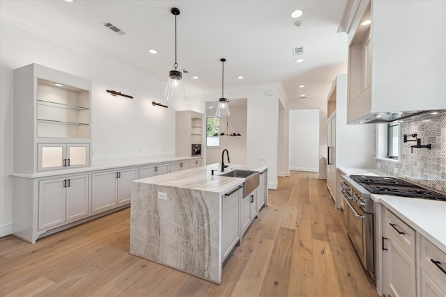 kitchen featuring high end stainless steel range, hanging light fixtures, a center island with sink, and white cabinetry