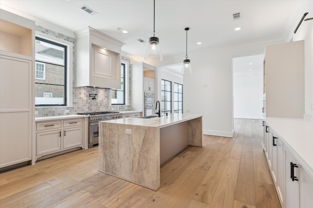 kitchen featuring a kitchen island with sink, stainless steel stove, hanging light fixtures, white cabinetry, and light hardwood / wood-style flooring