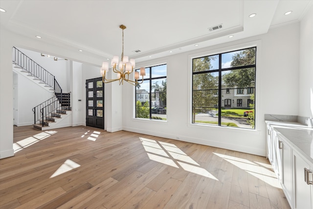 unfurnished dining area featuring light hardwood / wood-style floors, a tray ceiling, an inviting chandelier, and a healthy amount of sunlight