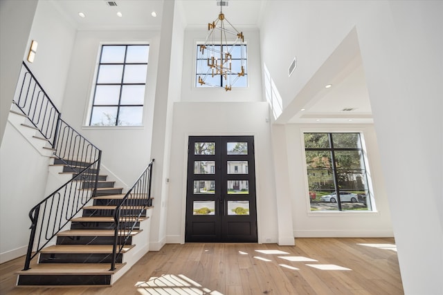 foyer with a towering ceiling, french doors, an inviting chandelier, and light hardwood / wood-style flooring