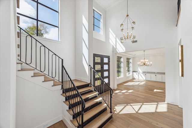 entryway featuring an inviting chandelier, light hardwood / wood-style flooring, a towering ceiling, french doors, and ornamental molding