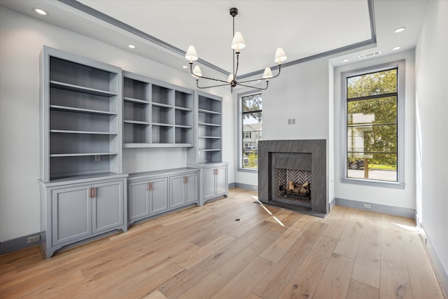 unfurnished living room featuring light hardwood / wood-style flooring, built in features, and a chandelier