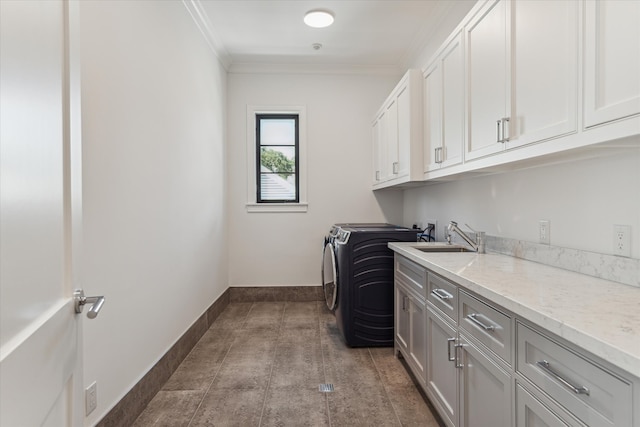 clothes washing area with ornamental molding, cabinets, sink, and washing machine and dryer