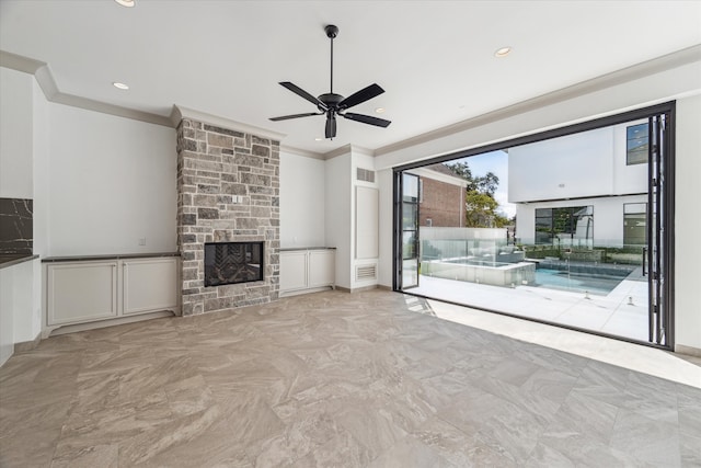 unfurnished living room with crown molding, ceiling fan, and a stone fireplace