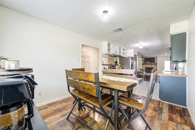 dining area featuring sink, a textured ceiling, light hardwood / wood-style flooring, and a brick fireplace