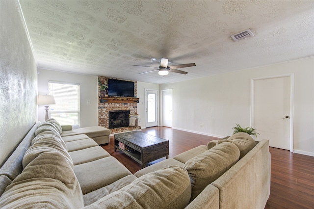 living room with ceiling fan, a textured ceiling, a brick fireplace, and dark hardwood / wood-style floors