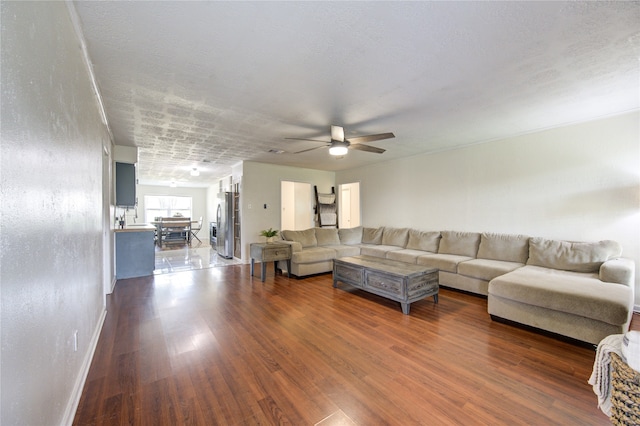 living room featuring dark wood-type flooring, ceiling fan, and a textured ceiling