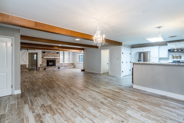 unfurnished living room featuring beam ceiling, light hardwood / wood-style flooring, a chandelier, and a fireplace