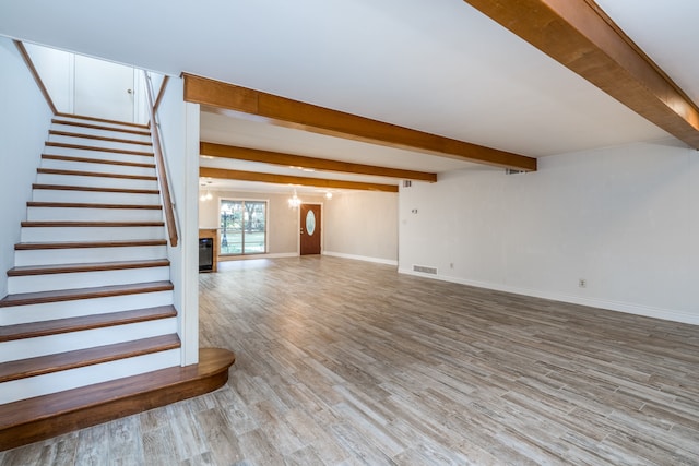 unfurnished living room featuring an inviting chandelier, beamed ceiling, and light wood-type flooring