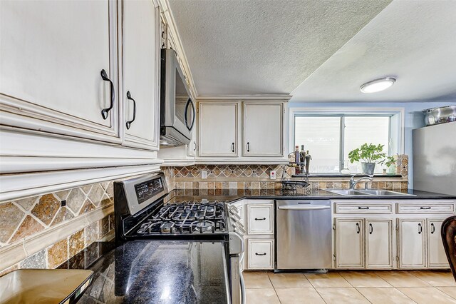 kitchen featuring dark stone counters, a textured ceiling, sink, appliances with stainless steel finishes, and light tile patterned floors