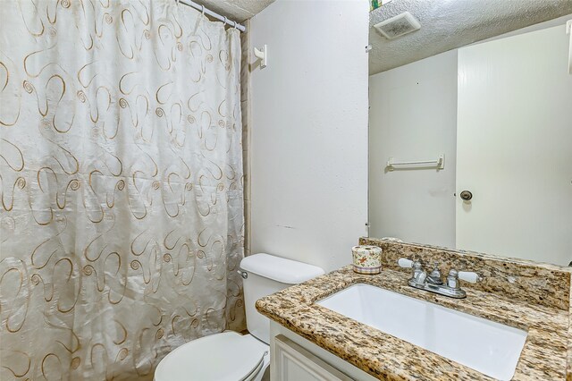 bathroom with a textured ceiling, vanity, toilet, and walk in shower