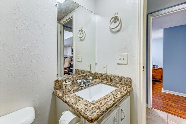 bathroom with wood-type flooring, a textured ceiling, vanity, and toilet