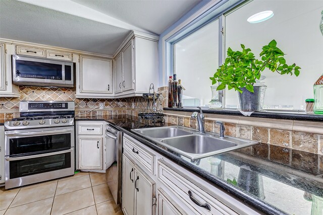 kitchen with light tile patterned floors, sink, stainless steel appliances, dark stone countertops, and decorative backsplash