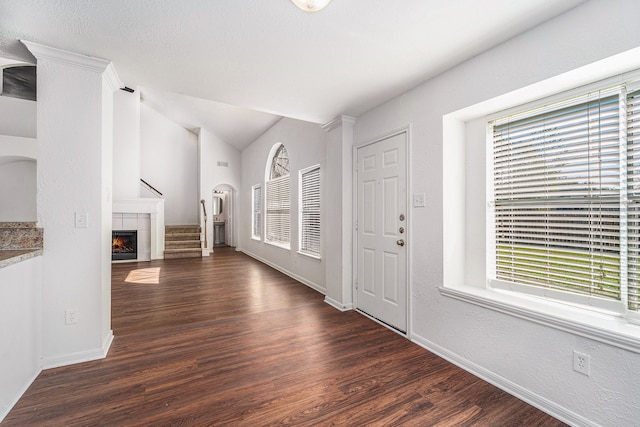 entryway featuring plenty of natural light, vaulted ceiling, dark wood-type flooring, and a tiled fireplace