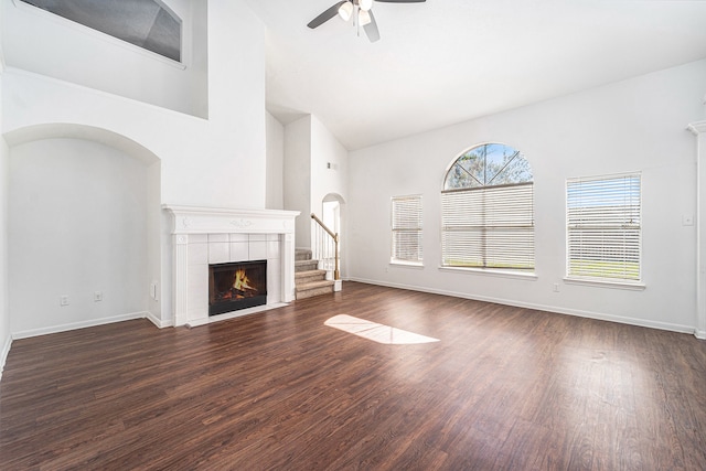 unfurnished living room with a tiled fireplace, ceiling fan, dark hardwood / wood-style flooring, and high vaulted ceiling