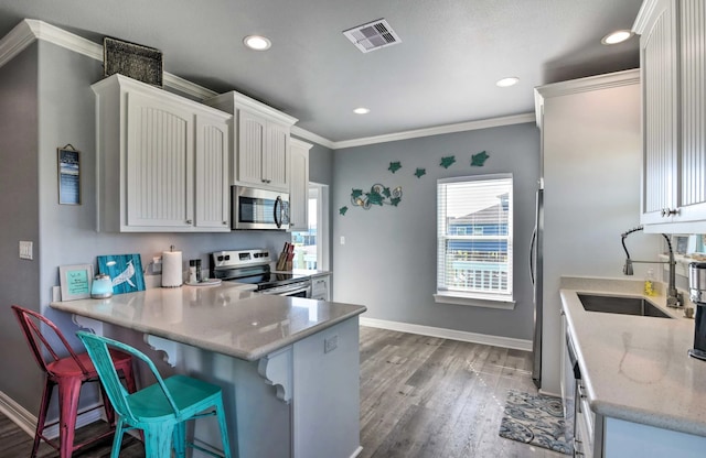 kitchen featuring kitchen peninsula, a kitchen breakfast bar, white cabinetry, light hardwood / wood-style floors, and stainless steel appliances