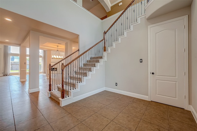 staircase with a towering ceiling, tile patterned floors, and a notable chandelier