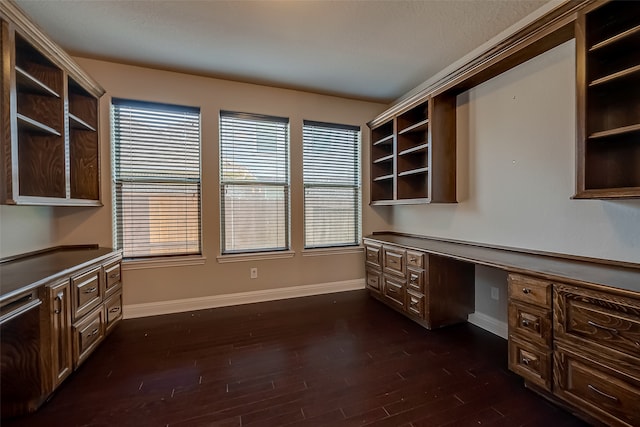 unfurnished office with dark hardwood / wood-style flooring, built in desk, and a wealth of natural light