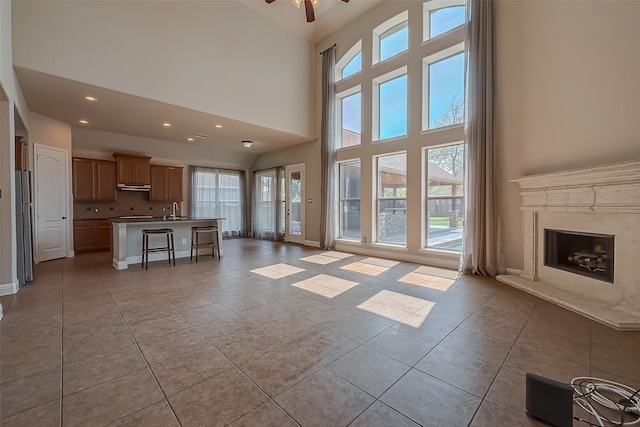 unfurnished living room featuring ceiling fan, light tile patterned floors, sink, and a high ceiling